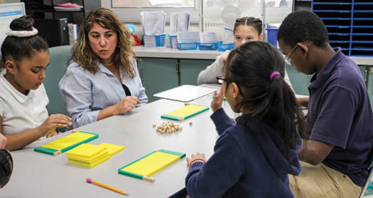 A small group of students engage in a hand-on math lesson with a teacher.