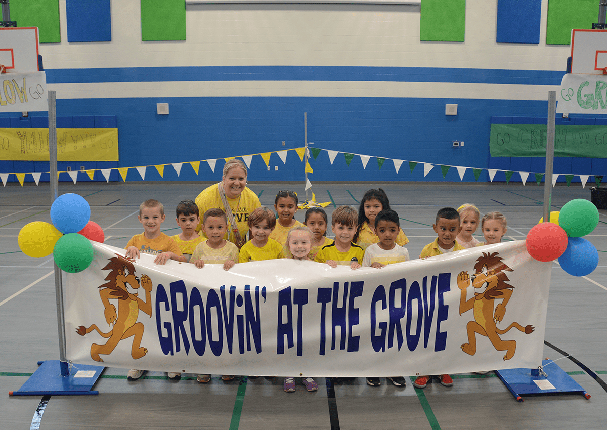 Young students and their teacher stand behind a banner that says, "Groovin' at the grove.