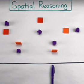 Red and blue blocks on a whiteboard placed above a pen with the words spatial reasoning.