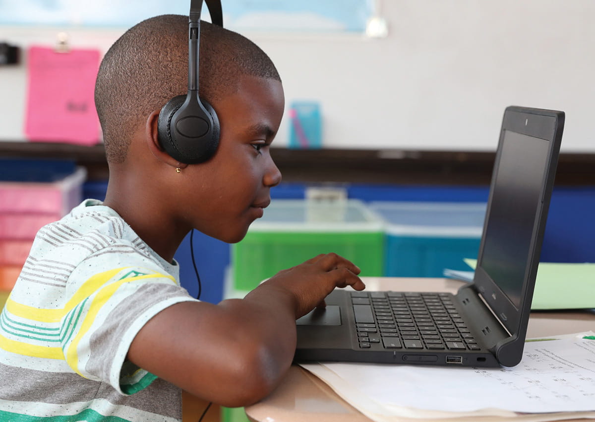 A student wearing headphones concentrates on a laptop screen.
