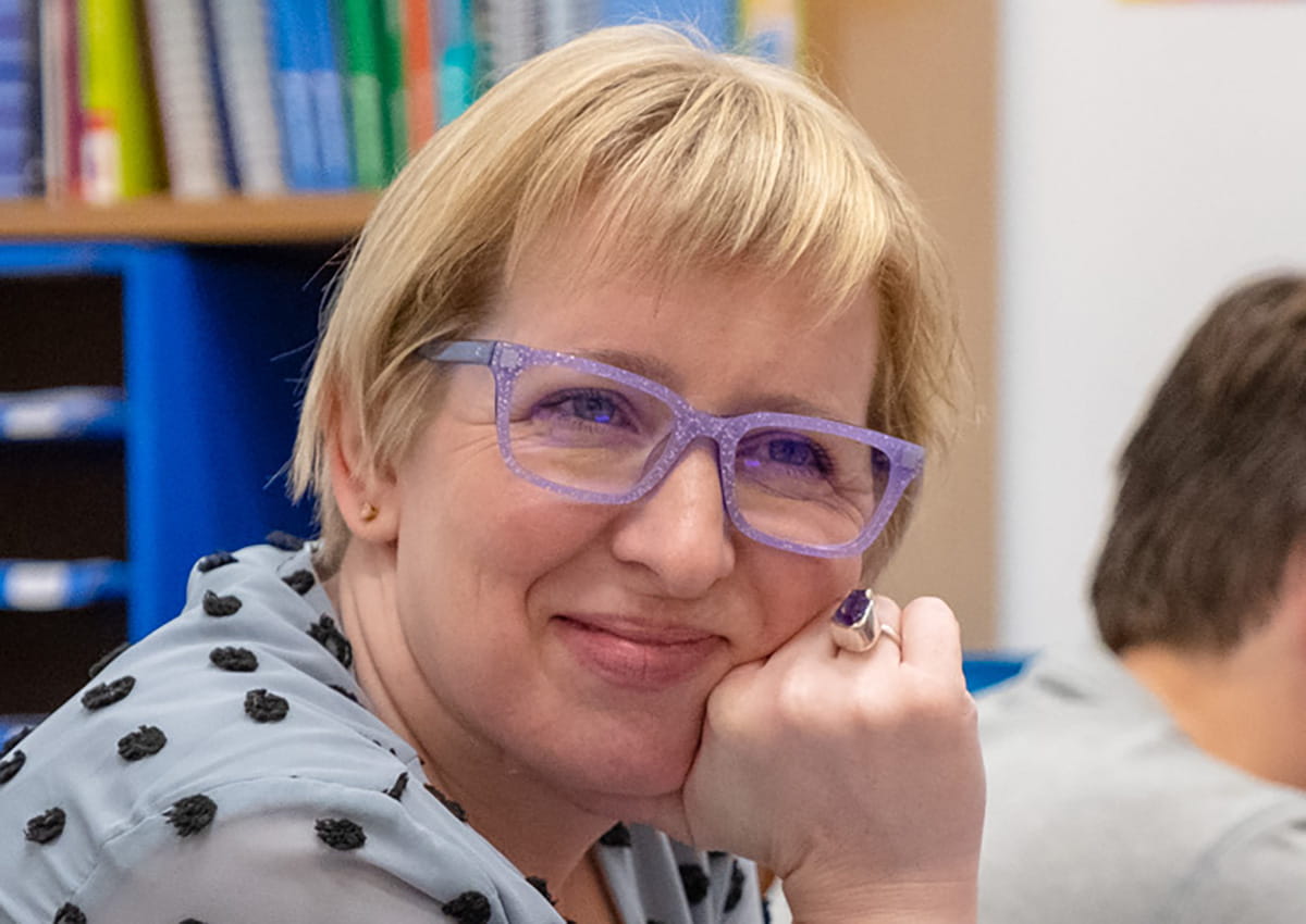 An educator wearing purple glasses smiles.