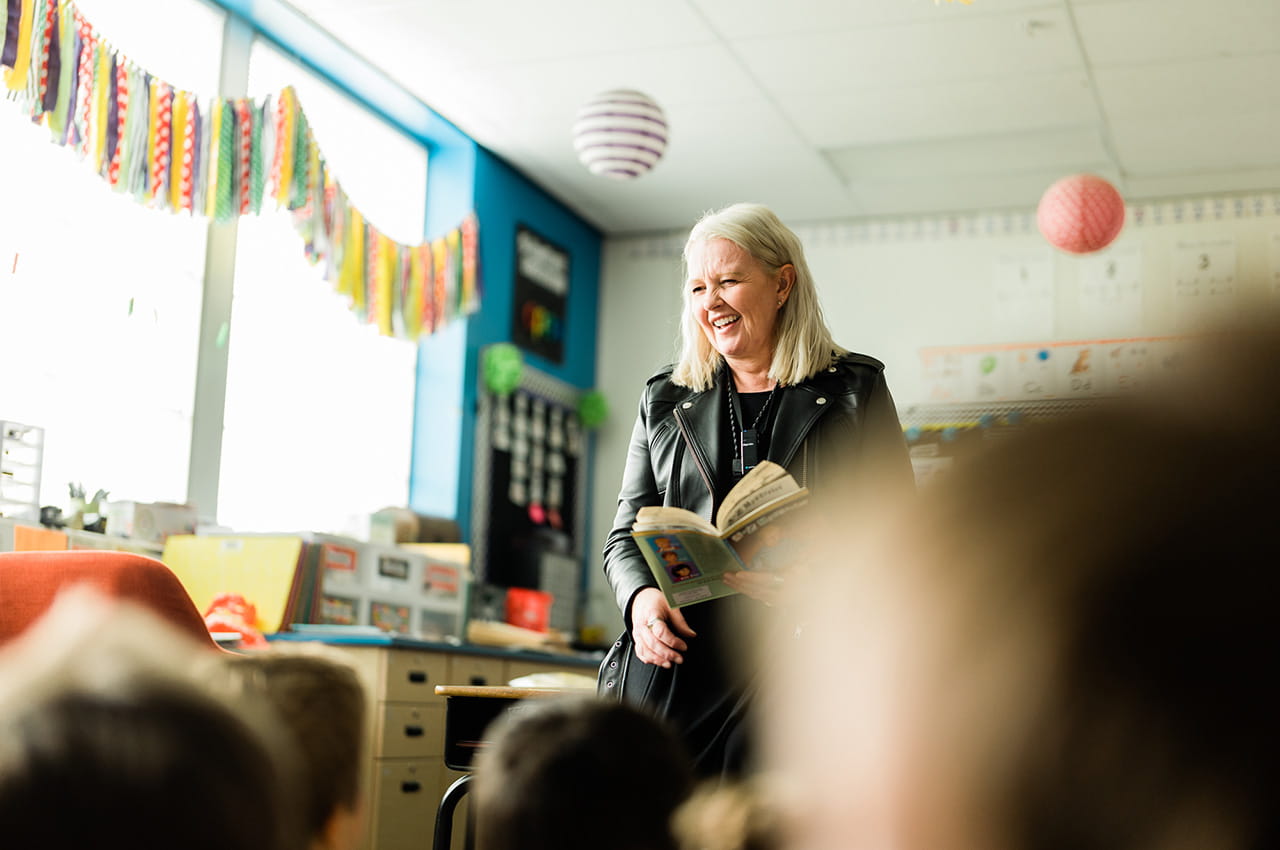 A teacher smiles as she reads to a class.