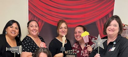 A group of teachers hold props while posing for a photo.