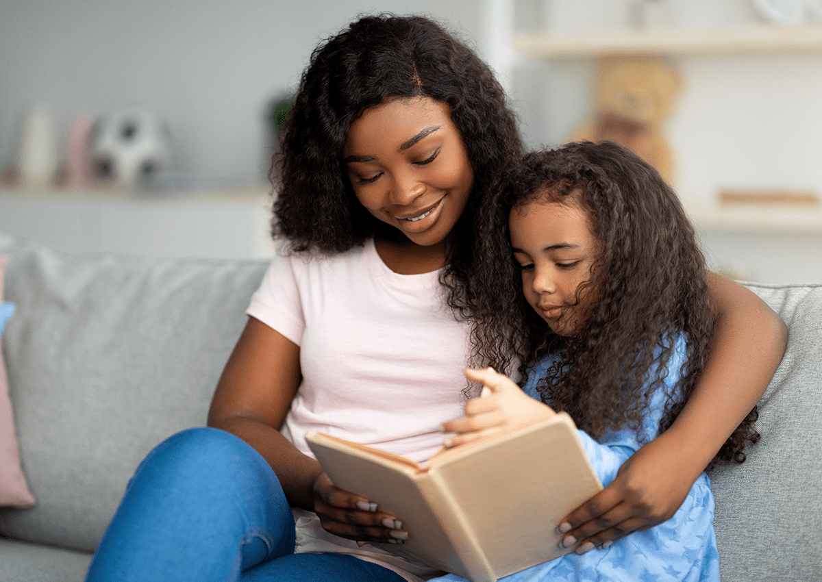 A mother and daughter are sitting together, reading a book.