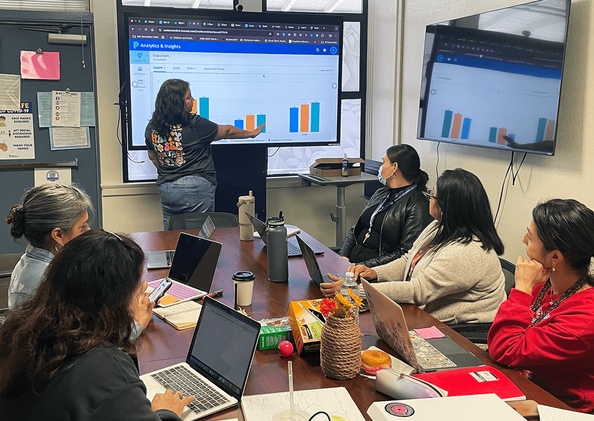 Educators look at a graph projected on a board during a meeting reviewing student data.