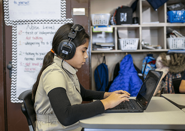 A student wearing headphones typing on a laptop.