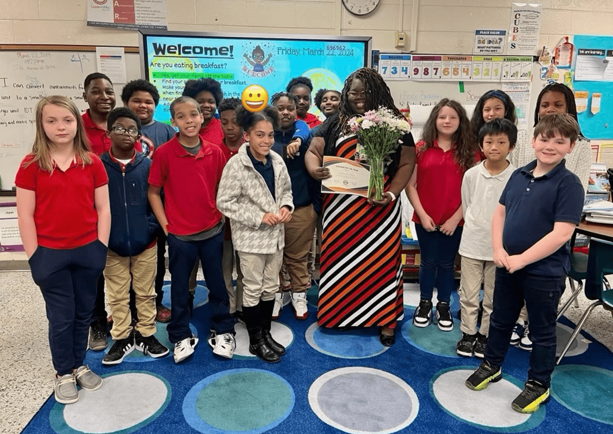 The author is holding flowers and a certificate, and is surrounded by smiling students.