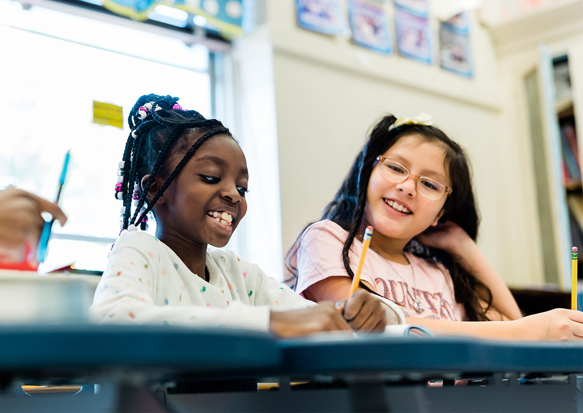 Two students smile at their desks.