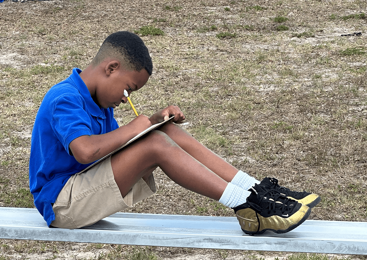 Kryk's student writing with a pencil outside.