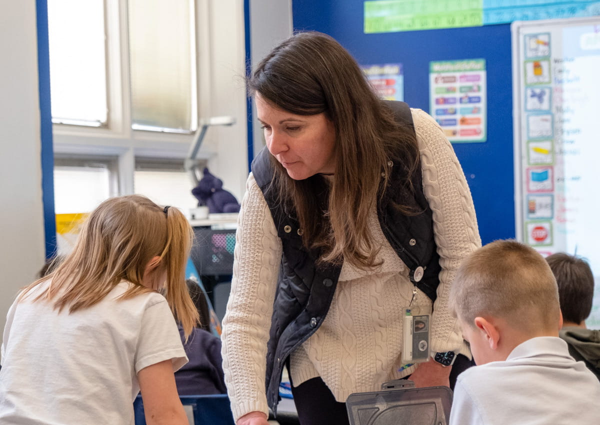 A teacher supports a young learner during a classroom activity.